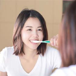 Woman brushing her teeth in a mirror