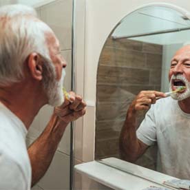 mature man brushing teeth for cost of dental implants in Garland