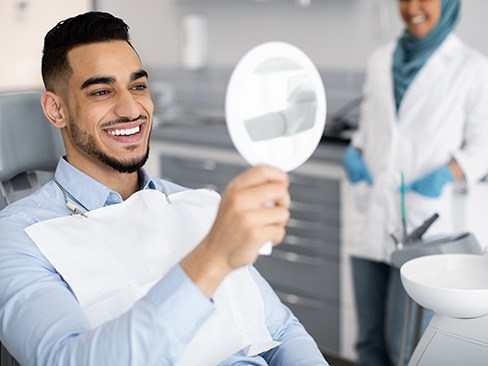 Man smiling at reflection in handheld mirror