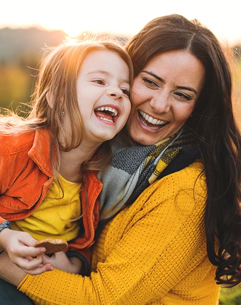 Smiling mother and child outdoors after receiving dental services