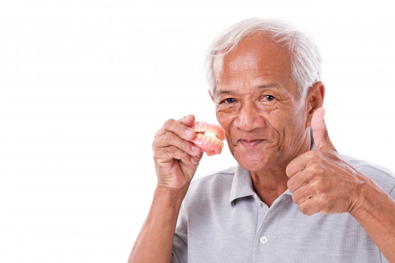 a man giving a thumbs up while holding his dentures
