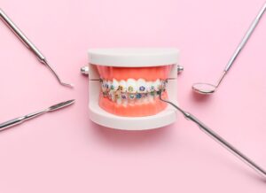 Model teeth with braces surrounded by dental instruments with pink background